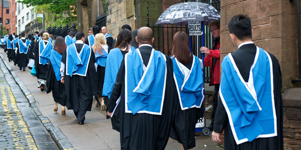 a group of graduates walks away from the barony, back view of gowns and hoods