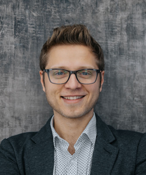 young man wearing glasses smiles at the camera