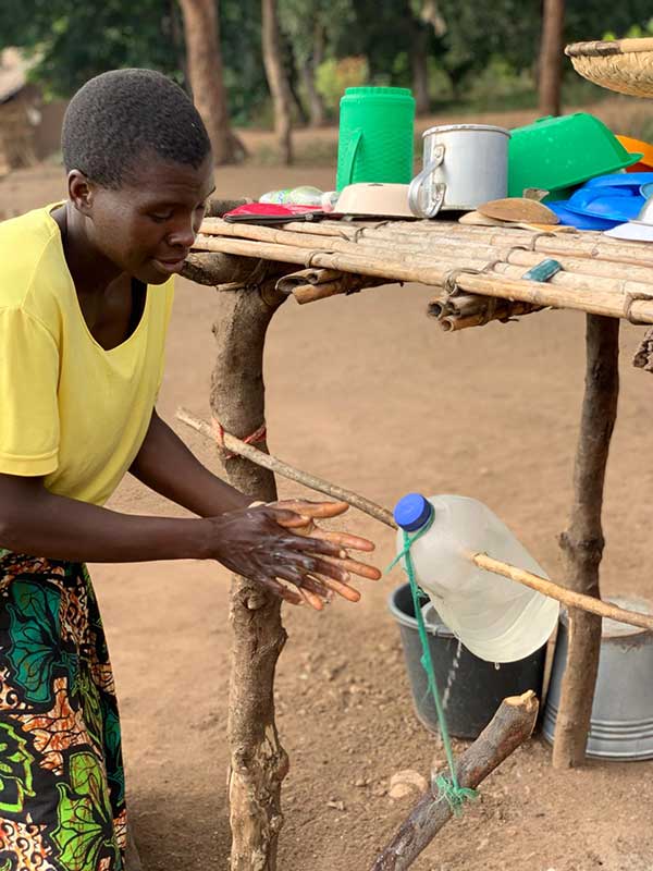 Person washing their hands in device built with a water bottle and string.