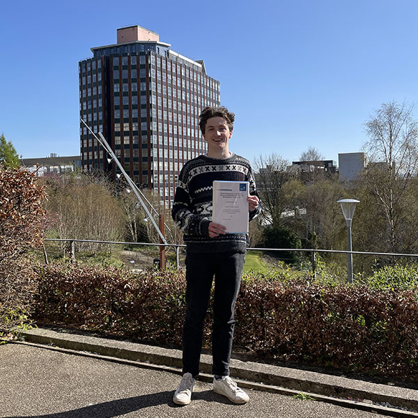 Alex Paterson holding his dissertation in Rottenrow gardens, with the Livingstone Tower in the background.