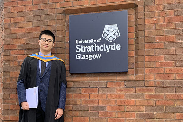 Xuran Xiao wearing graduation gown, next to a University of Strathclyde sign.