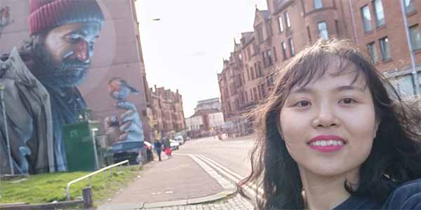 Vietnamese student Tien Thuy Quach standing in front of an artistic wall mural 