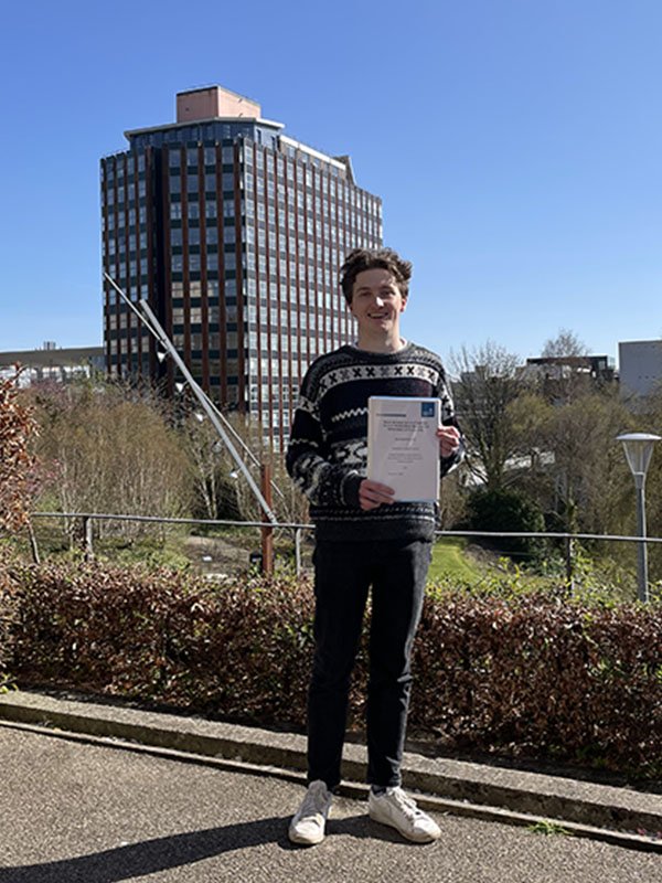 Alex Paterson holding his Dissertation in Rottenrow Gardens with the Livingstone Tower building in the background.