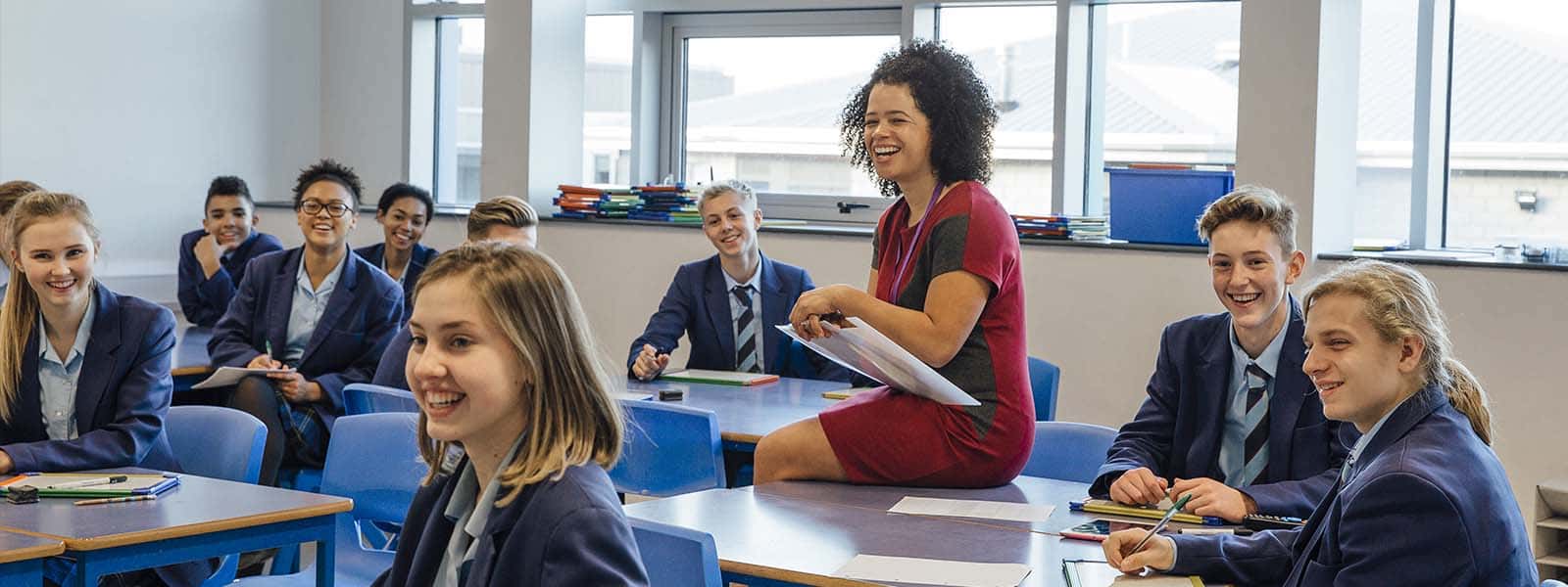 Teacher sitting on a desk laughing with pupils