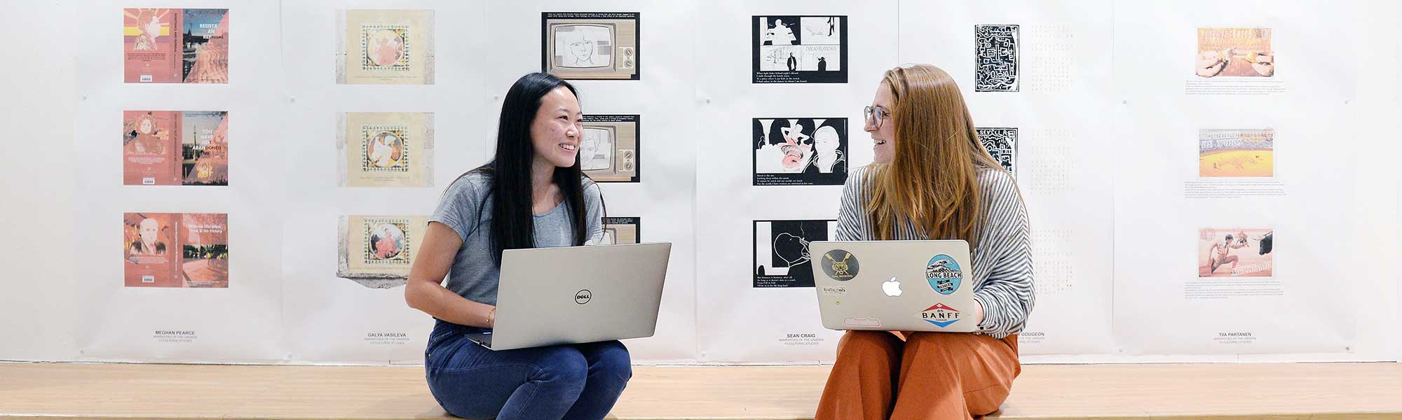 two students sitting apart with laptops smiling at each other