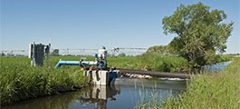 A pump in a stream provides water to a pivot irrigation system that waters a field of crops.