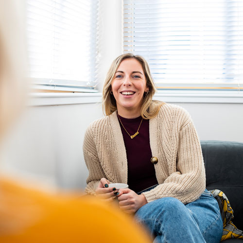 Catherine Quinn sits in an armchair with a mug in her hands, smiling off the camera