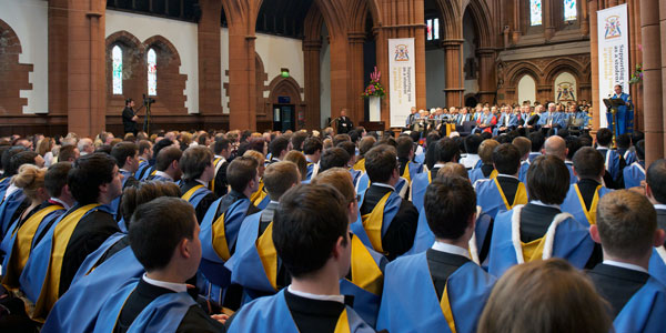 a view from behind students wearing graduation gowns at their graduation ceremony facing the stage