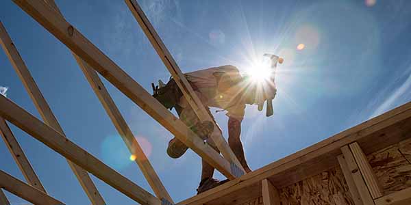 Construction worker positioning a piece of frame work, a roof truss onto a building structure against a sunny blue sky