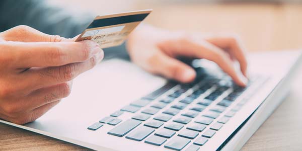 Close-up of hands holding credit or debit card and entering information on laptop
