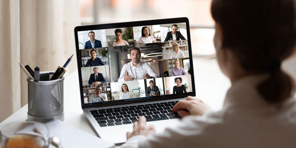 a woman sits at a computer talking to colleagues on video chat