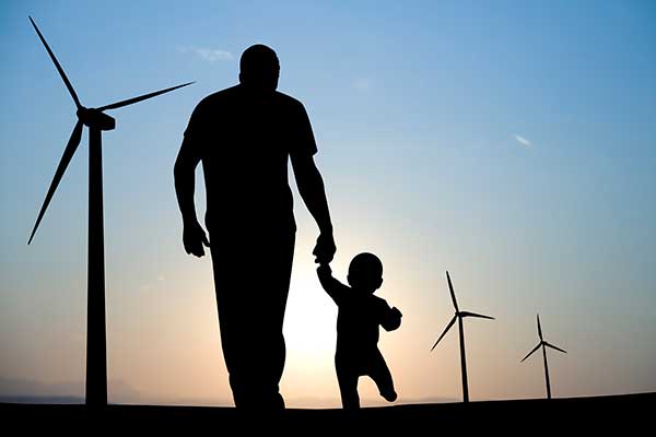 Silhouette of a father and son walk through a wind farm. 