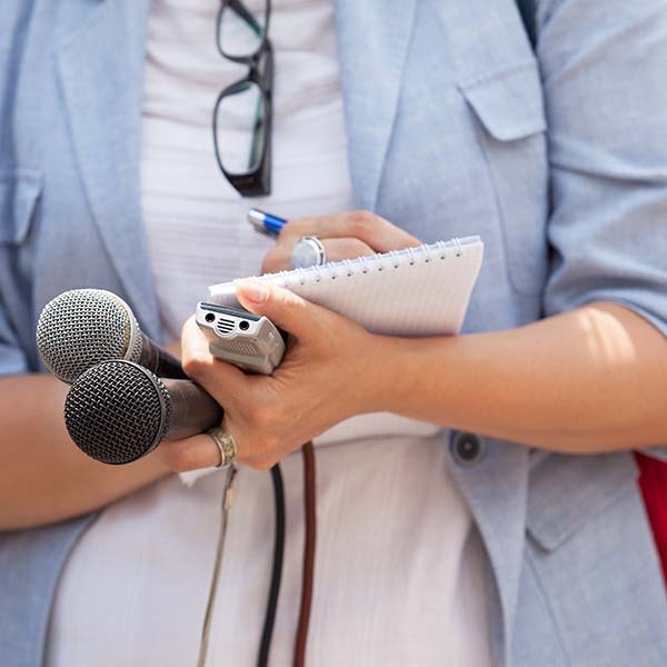 Journalist holds microphones and Dictaphone while taking notes/