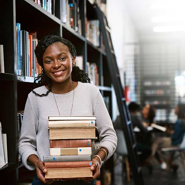 Student holding books in library.