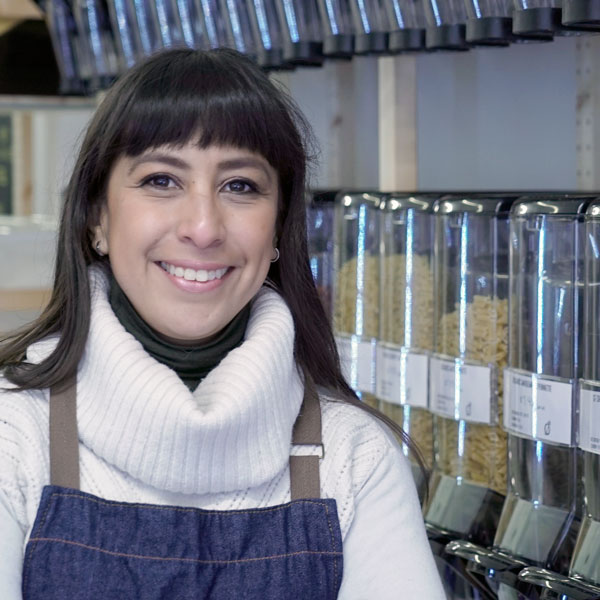 Pilar, owner of The Good Choice store, standing in the store in front of her bulk bins, smiling at the camera
