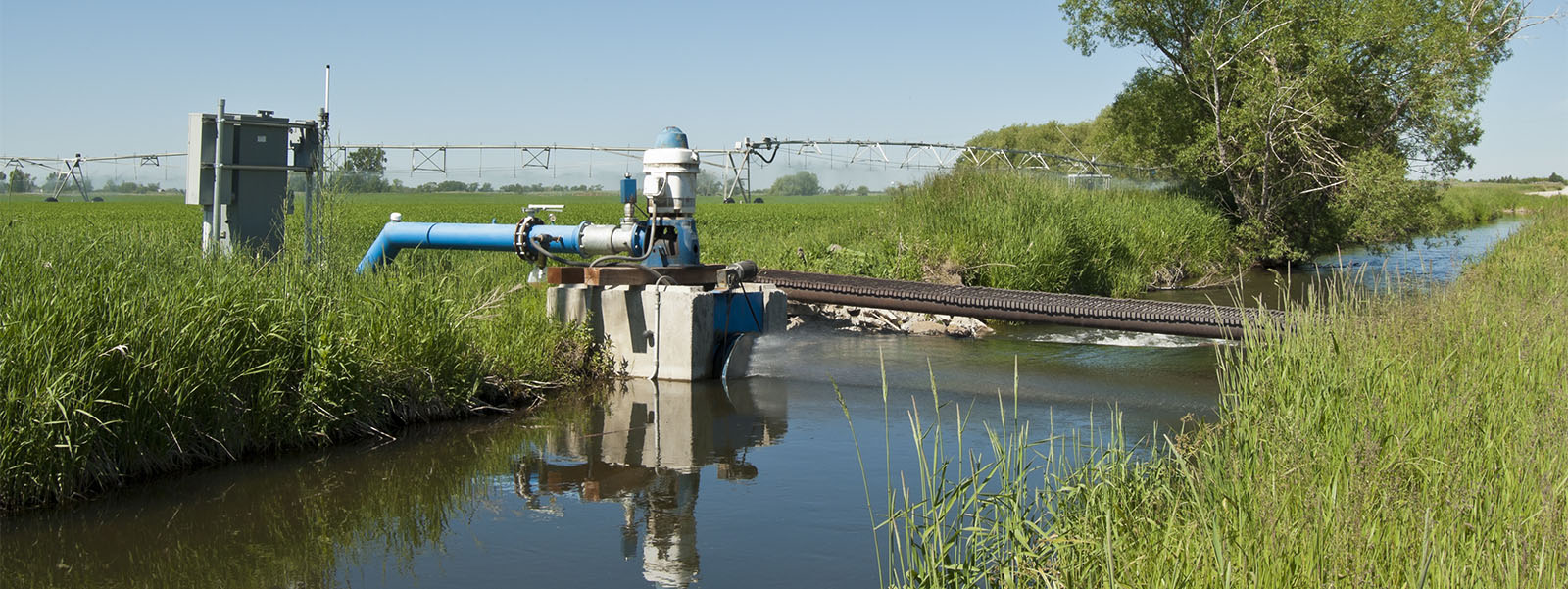 A pump in a stream provides water to a pivot irrigation system that waters a field of crops.