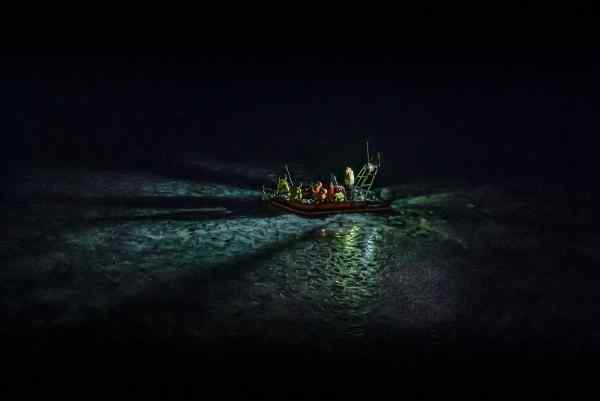 An orange rib in the sea at night with a number of passengers wearing life jackets