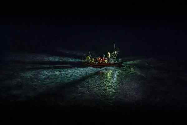 An orange rib in the sea at night with a number of passengers wearing life jackets An orange rib in the sea at night with a number of passengers wearing life jackets