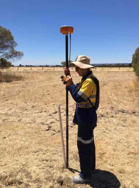 A woman stands in a field holding a long measuring tool A woman stands in a field holding a long measuring tool