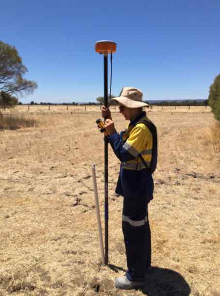 A woman stands in a field holding a long measuring tool