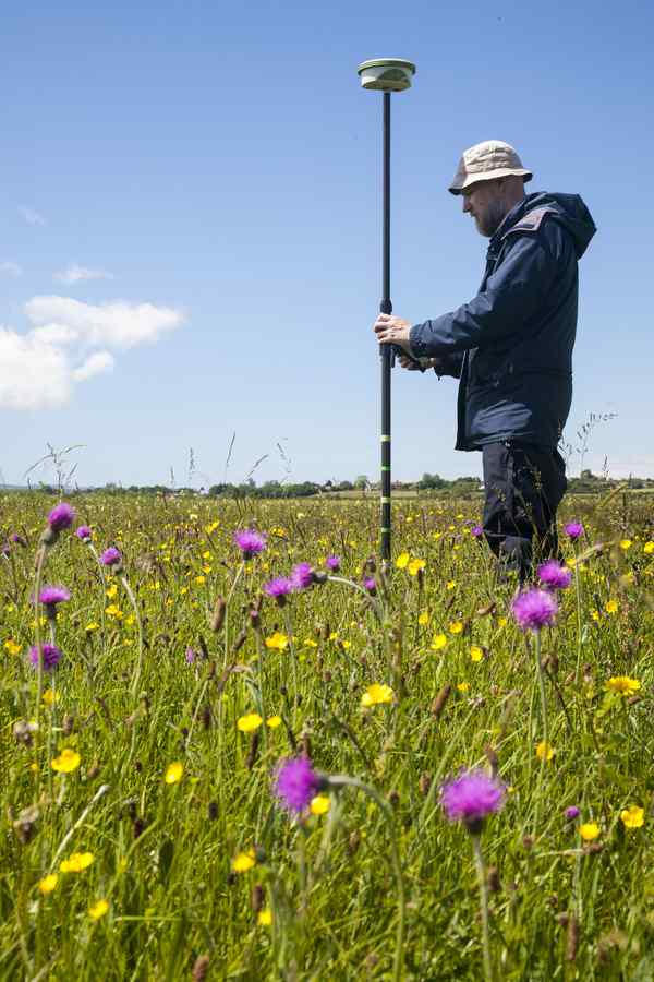 A person standing in a green field holding a tall measuring devide