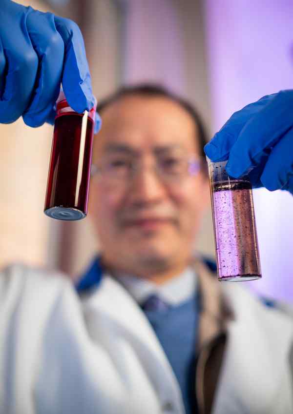 A scientist holds up a vial of red liquid and a vial of clear liquid