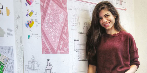 Female student stands leaning against a decorative wall, smiling at the camera