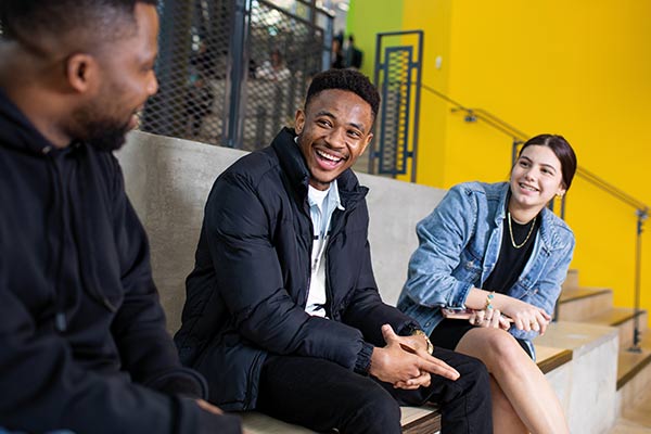 Three students sitting on stairs in conversation smiling