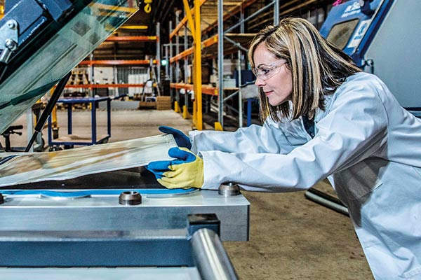 Machine factory worker in safety goggles and gloves laying a piece of sheet metal on a press machine