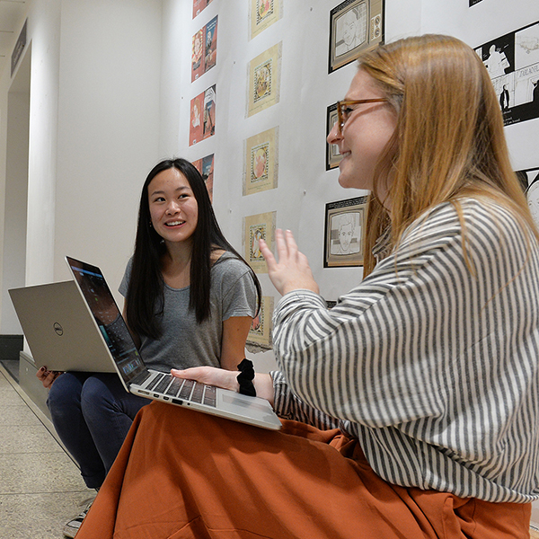 Two women discussing work while holding their laptops