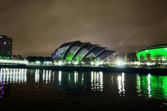 The site of COP26 in Glasgow at night, with green light reflected in the river Clyde.