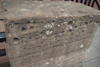 A sandstone block with round marks caused by coins.
