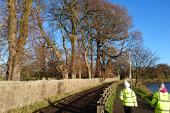 Two people with high visibility jackets walk along a flood protection scheme.