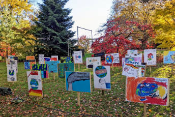 Children’s drawings are attached to a word board and peg and they are stuck on the ground.