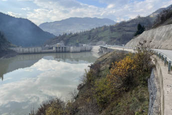 A dam of a hydropower project reflects the clouds and surrounding landscape in the water surface.