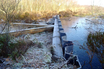 A small dam holds peat soil in winter. Ice crystals can be seen in the vegetation and the structure.