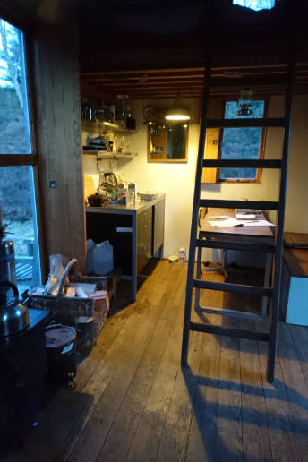 The inside of the Inshriach Bothy in the Cairngorms, showing a desk, a widow, a kitchen cabinet and a ladder.