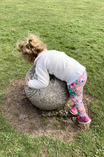 A little girl holds a stone sphere in a park, symbolising the world.
