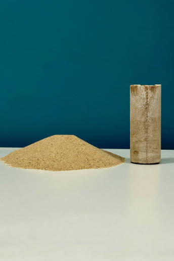 A pile of sand is next to a cylinder of sandstone.