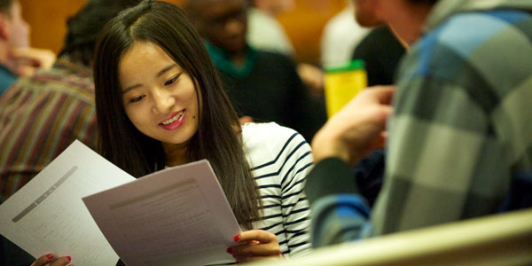 a female student looks at A4 pages in her hands with a smile on her face
