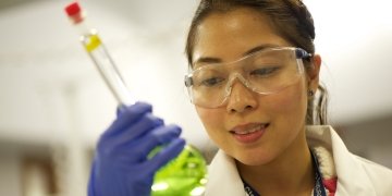 Laboratory Researcher Looking At Flask of Green Liquid 360x180