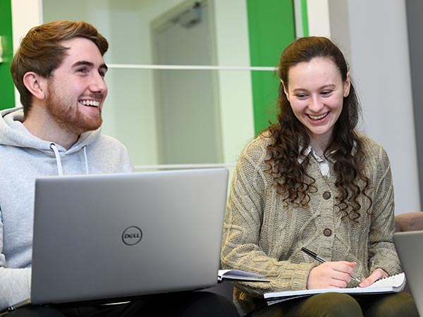 Two students in a study area, one with a laptop.