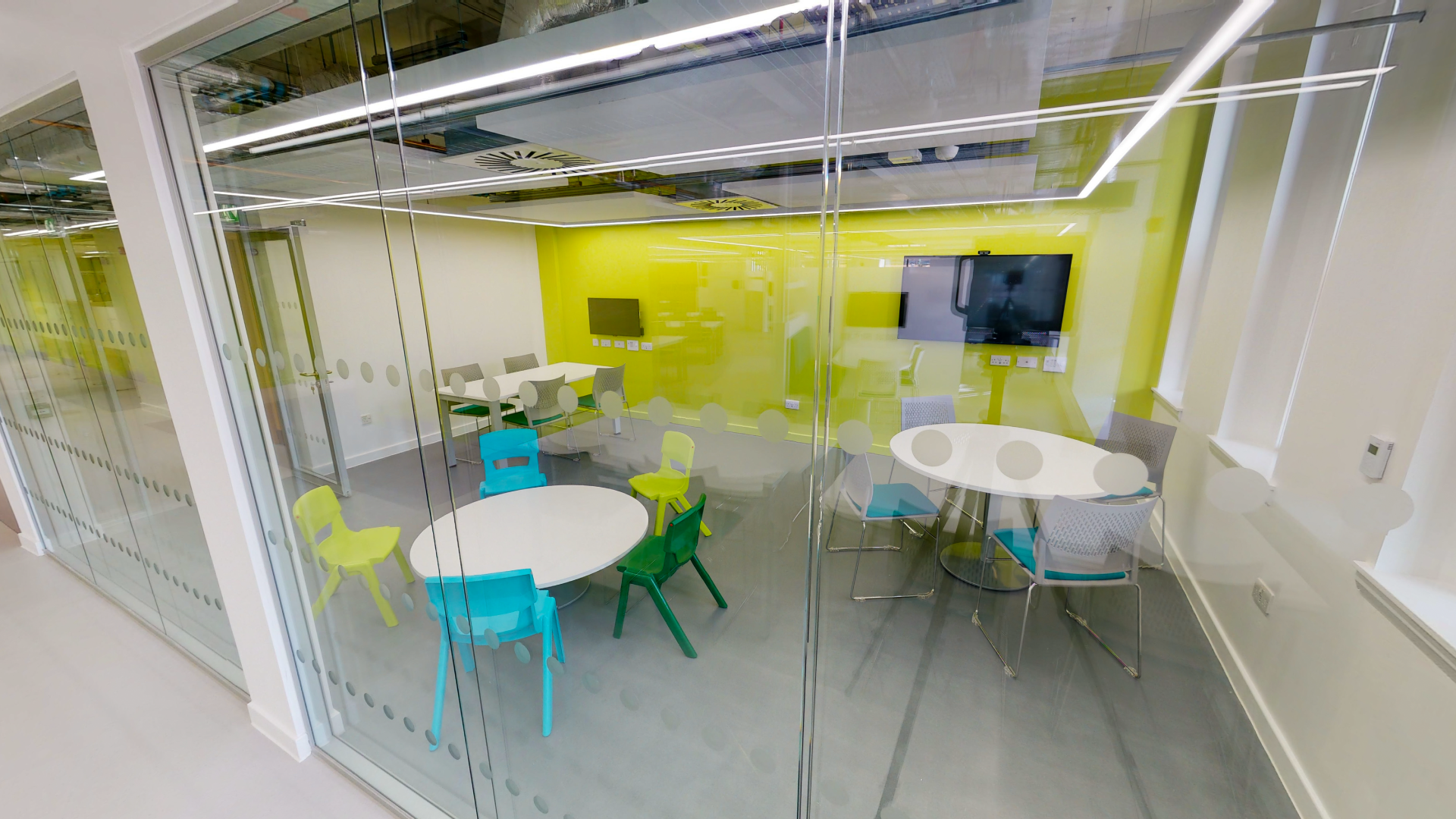 The Family Study Room in the Library as viewed from outside the room with three tables and chairs around the tables.