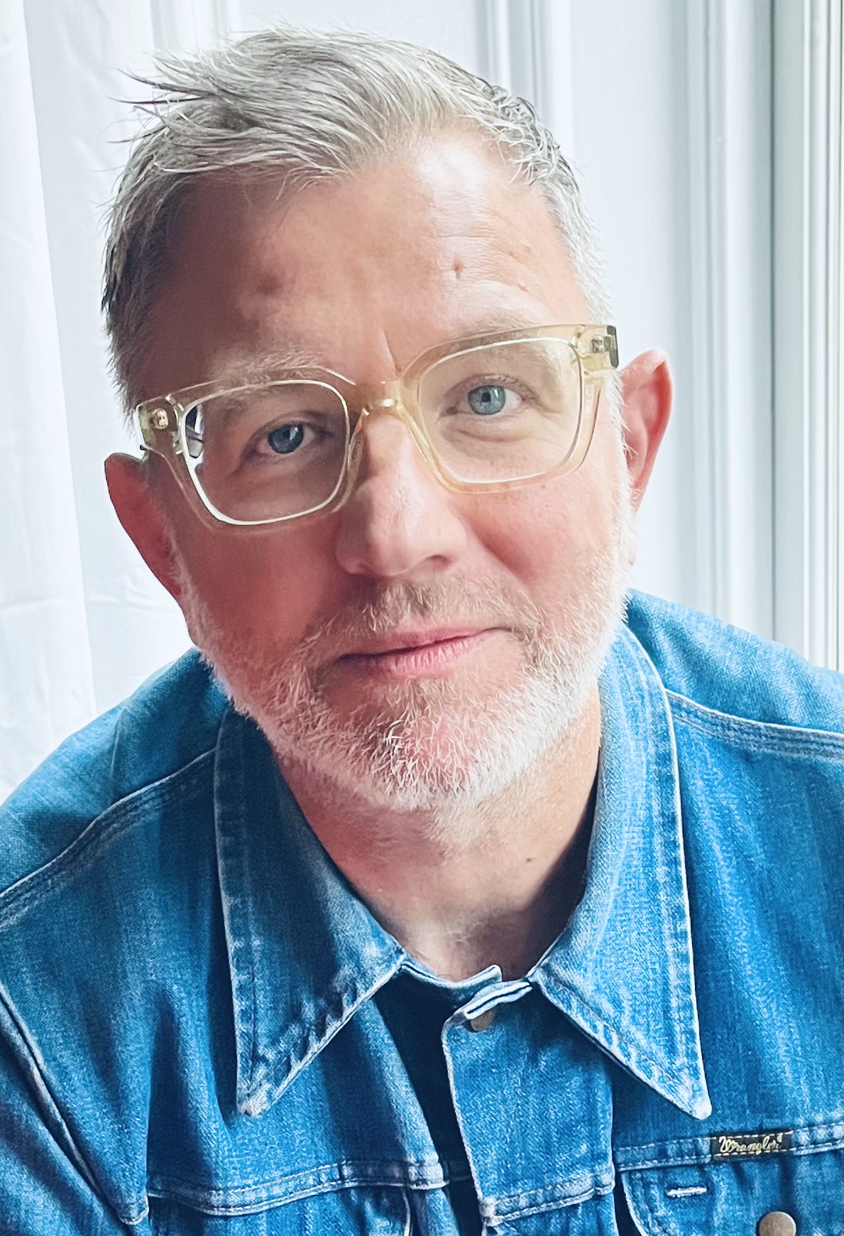 A smiling man wearing a blue shirt and glasses.