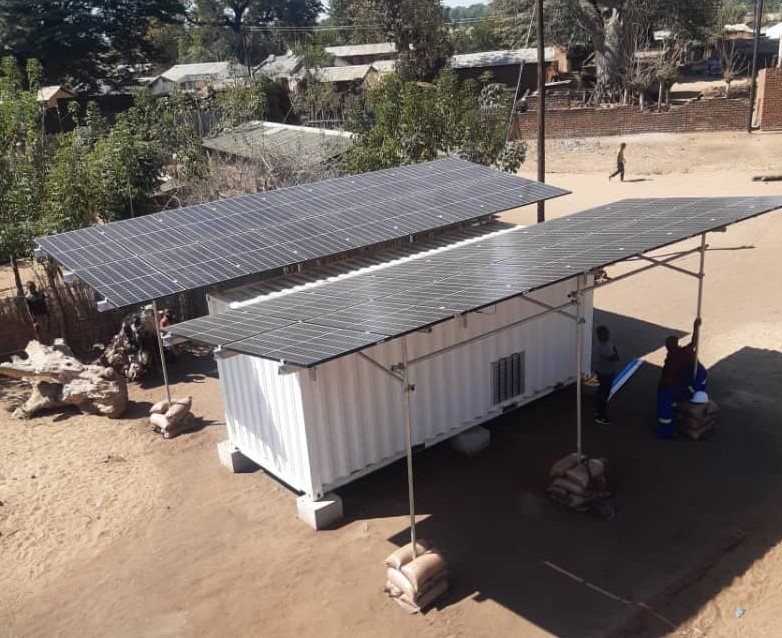 A small white building with solar panels on the roof in a rural setting in Malawi