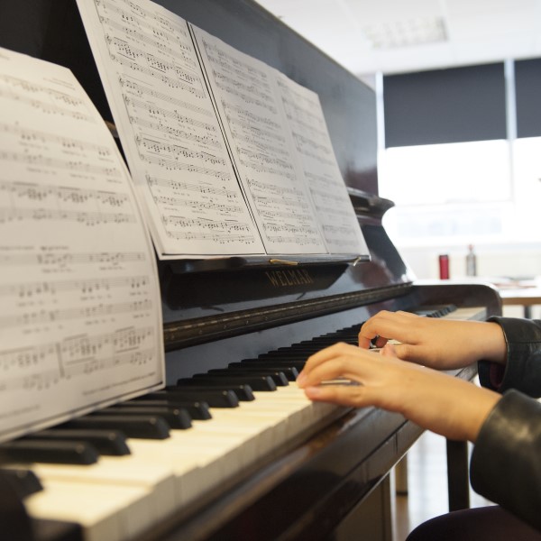 A piano keyboard with sheet music and pianist's hands