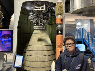 Male student in a University of Strathclyde hoodie in front of a rocket at the Japanese Space Agency.