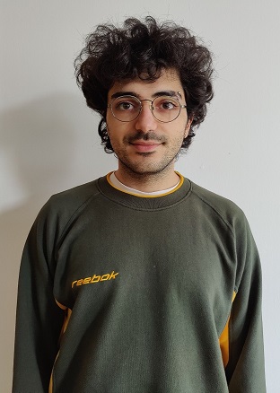 A dark haired student, wearing glasses and a grey and yellow sweatshirt standing in front of a white background.